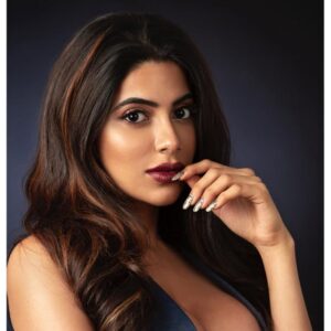 Elegant woman with wavy hair and bold makeup posing confidently with hand near lips